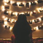 a woman sitting in front of pictures framed in fairy lights